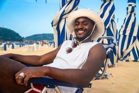 Young african male with straw hat and sunglasses hanging on his shirt smiling while sitting in a