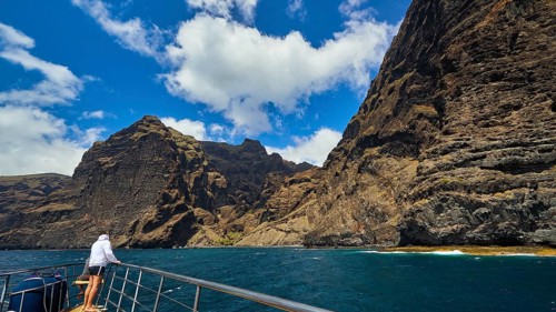 Los Gigantes, person on a boat admiring the impressive rock formations under a partly cloudy sky,