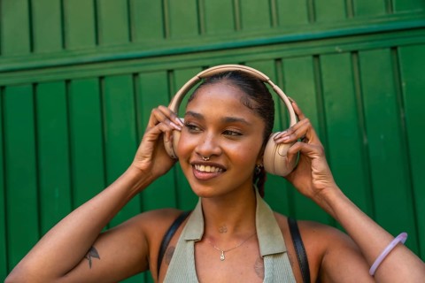 Young woman smiling while adjusting her wireless headphones, enjoying music and leisure time