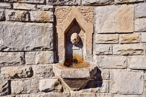 Wall fountain, public drinking water dispenser, sculpture of a fish, sandstone wall, sunny,