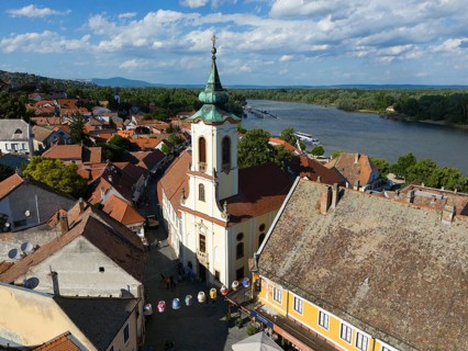 Urban view near the river and a church in the center, lively with people, under blue sky, aerial