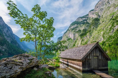 Wide angle view of the wooden boat shed at Obersee lake with a green tree on a rocky outcrop,