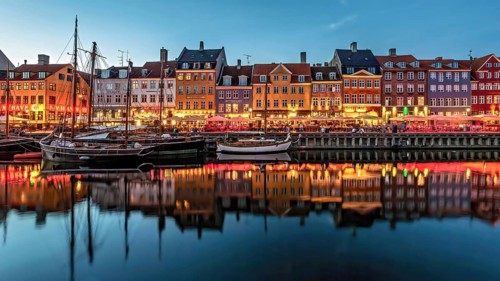 Abend am Hafen mit beleuchteten, bunten Gebäuden und ruhig liegenden Booten, Kopenhagen, Dänemark,