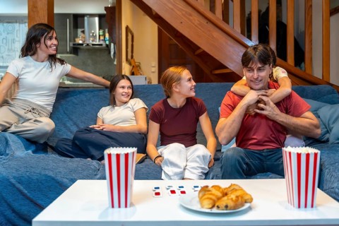 Family members sitting on a couch in their living room, watching a movie, eating popcorn and