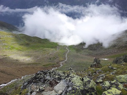 View of a valley with flowing clouds surrounded by mountains and green meadows, E5, hiking in the