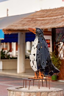 Close-up view of a metallic penguin sculpture against an urban background, statue on the beach