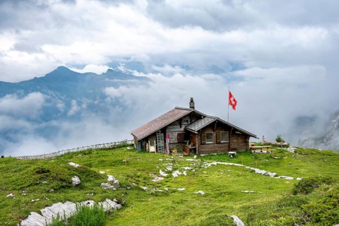 Small mountain hut Suls-Lobhornhütte with Swiss flag, cloudy mountain landscape, Bernese Alps,