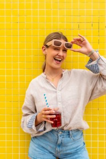 Happy young woman winking, laughing, and holding a refreshing iced drink, standing in front of a
