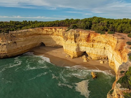 Drone view of cliffs above Benagil Cave in Algarve, Portugal, with a sandy cove, limestone rock