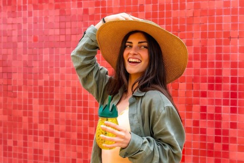 Woman smiling brightly and posing in a straw hat, holding a refreshing pineapple shaped drink