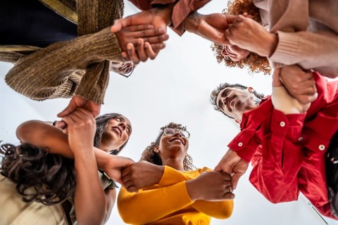 Diverse group standing in a circle, holding wrists and looking up with smiles, conveying unity,