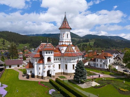 Ornamental Orthodox Church with a pointed tower surrounded by mountains and trees, aerial view,