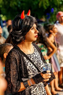 Woman with small horns on wig looks interested in one direction at night, visitor to a festival in