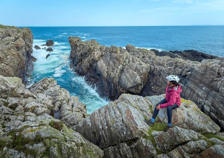 Nice senior woman resting during a bicycle tour in the rocky cliffs of Strathy Point in northern
