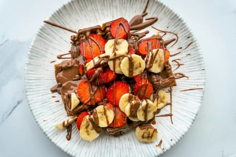 Close up top down view massive, high-calorie waffle topped with strawberries, bananas, and