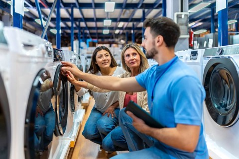 Sales associate helping a mother and daughter select a new washing machine at a home appliance
