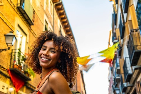 Happy black woman with afro hair smiling while walking through a colorful street in madrid,