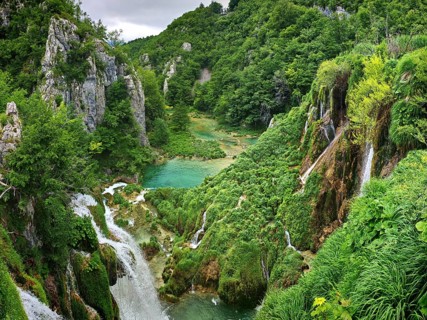 Waterfalls flow into turquoise lakes surrounded by thick forests and rocks, Plitvice Lakes National