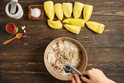 Cook adds minced garlic in bowl with rice, ground meat and spices. Green peppers are cut and placed