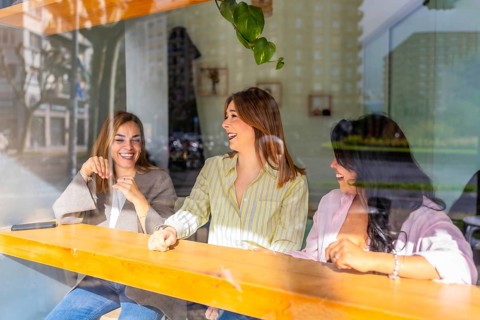 Three happy friends enjoying conversation and coffee together in a vibrant cafe, visible through a