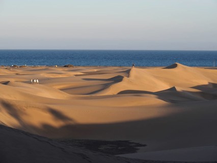 The setting sun bathes dunes in warm light, shadows form on the sand, dunes of Maspalomas, Gran