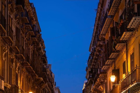 City street illuminated in the evening with tall old buildings and lantern light under clear sky,