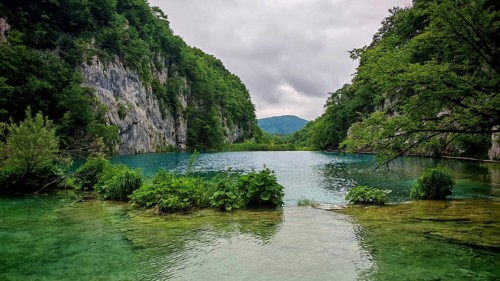 A calm turquoise lake nestles between wooded mountains and rocky shores, Plitvice Lakes National