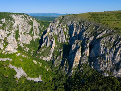 Natural rough rocks surrounded by a green landscape bordering a blue sky, aerial view, Cheile