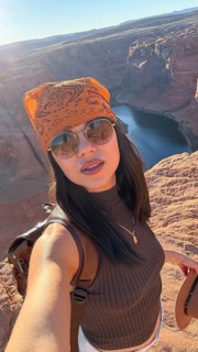 Young woman in bandana and sunglasses stands on sandstone cliff at horseshoe bend, overlooking the