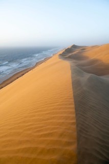 Sand dunes and sea in evening light, wind blowing sand across the dunes, view of the Atlantic coast