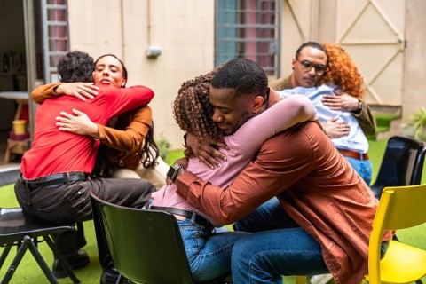 Diverse people participate in a group therapy session, hugging each other and offering emotional