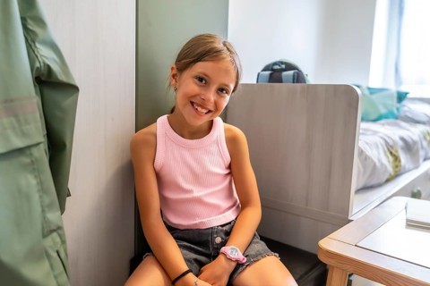 Young caucasian girl smiles happily while sitting on floor inside her bright modern bedroom with