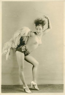 A woman wearing feathers and shorts in a dancing pose with a lively expression