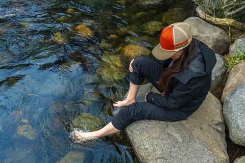 Woman dipping bare feet into a shallow, clear mountain river, enjoying the refreshing cool water