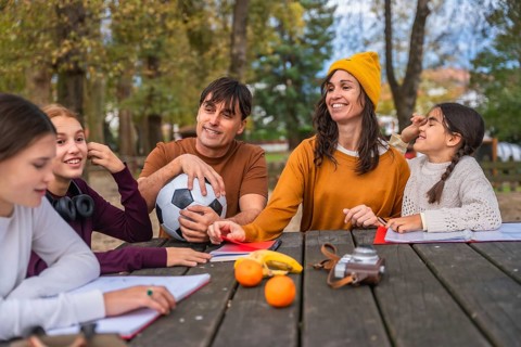 Happy family gathered at a wooden picnic table in a sunny park, enjoying autumn leaves, healthy