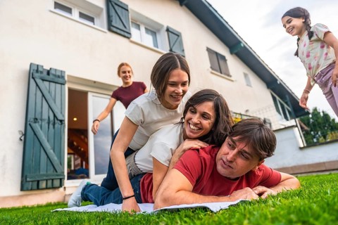 Happy family playing in their backyard, parents give piggyback rides to smiling children on green
