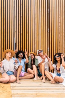 Diverse group of young adult friends sitting on a wooden deck next to a modern slatted wall,