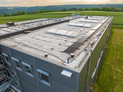 Industrial building with solar panels on the roof, surrounded by green fields, PV assembly, Perrot