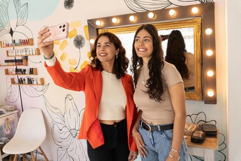 Makeup artist and satisfied client smile while taking a selfie together after a successful makeup