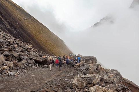 People gather on a foggy, rocky mountain road with a tractor in the background, rockslide on the