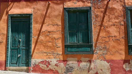 Weathered orange house wall with green windows and an old door, capital city, Santa Cruz de
