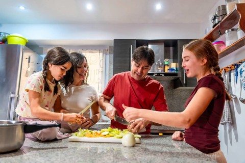 Parents and their two daughters are sharing a happy moment preparing a healthy meal, slicing and