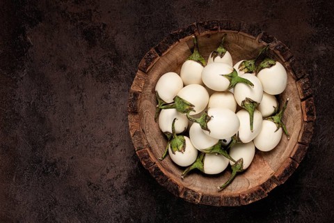 White mini eggplant, in a wooden bowl, on the table, close-up