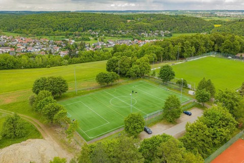 Aerial view of a sports field with a green soccer field, surrounded by trees, in a green landscape