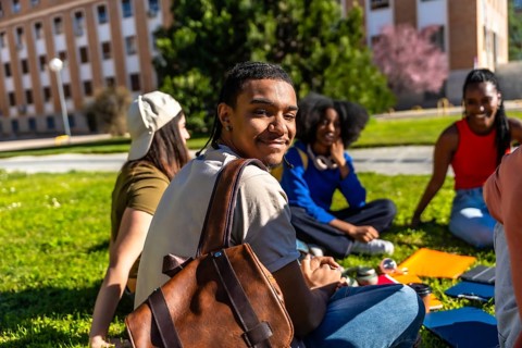 Group of diverse university students smiling and sitting on a green lawn, enjoying an outdoor study