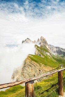 Wooden safety railing fence overlooking dramatic mist covered Seceda mountain peaks steep cliff