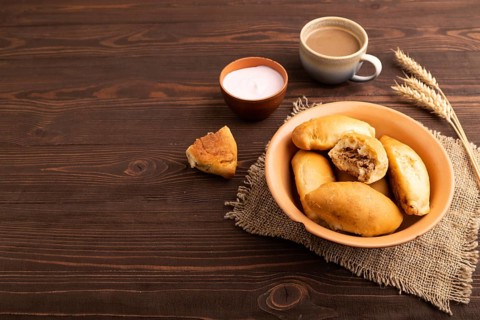 Homemade pies with jam and curd, cup of coffee, on brown wooden background with linen textile, copy