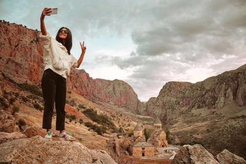 Happy excited female tourist takes a selfie photo against the background of the famous Noravank