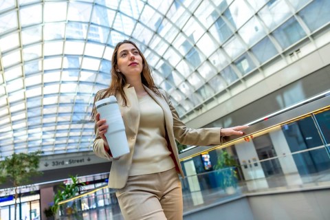 Professional businesswoman commuting to work, holding a reusable cup while moving on an escalator