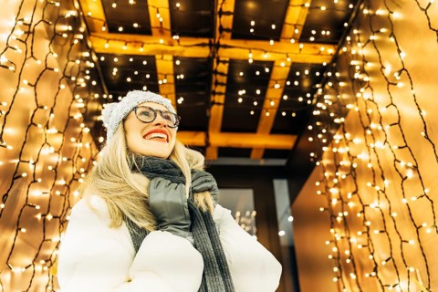 Young woman in winter clothing looking up under festive lights. A woman wearing a white winter